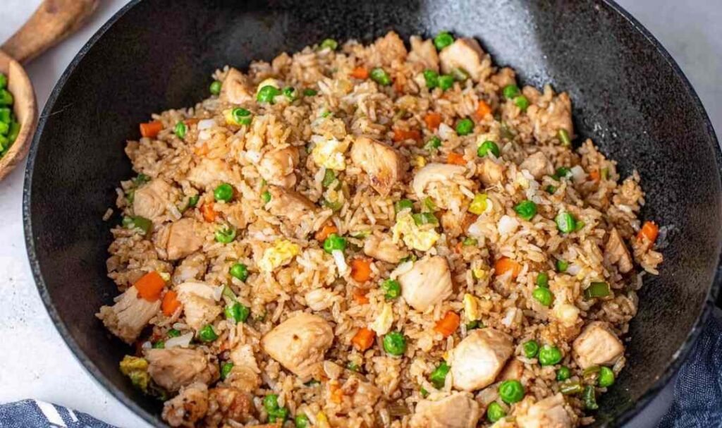 Chicken fried rice with tender chicken breast, scrambled eggs, peas and carrots cooking in a large skillet