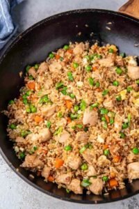 Chicken fried rice with tender chicken breast, scrambled eggs, peas and carrots cooking in a large skillet