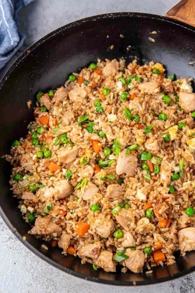 Chicken fried rice with tender chicken breast, scrambled eggs, peas and carrots cooking in a large skillet