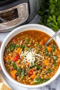 Close-up of a bowl of Instant Pot lentil soup with wilted spinach, smoky broth, and grated Parmesan on top
