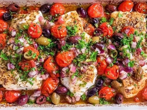 Mediterranean baked cod with kalamata olives, cherry tomatoes, and garlic in a white baking dish