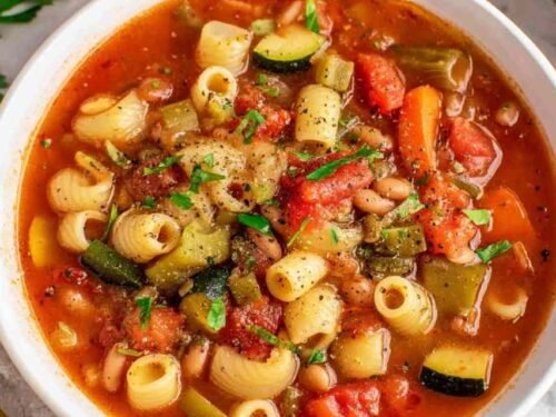 Bowl of minestrone soup with vegetables, beans, and pasta topped with Parmesan cheese