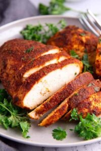 Juicy oven baked chicken breast sliced against the grain on a wooden cutting board, seasoned with paprika and herbs