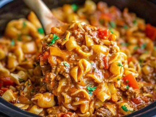 Bowl of slow cooker taco pasta with seasoned ground beef, shell pasta, cheddar cheese, sour cream, and fresh cilantro