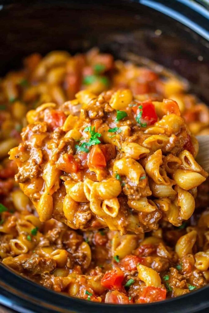Bowl of slow cooker taco pasta with seasoned ground beef, shell pasta, cheddar cheese, sour cream, and fresh cilantro
