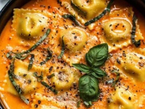 A bowl of Easy Tuscan Ravioli Soup topped with grated Parmesan cheese and served with crusty bread on the side