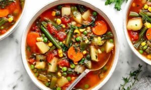 Easy Vegetable Soup Bowl of easy vegetable soup with carrots, potatoes, green beans, and parsley on a rustic wooden table