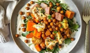 Colorful glow bowl recipe with roasted cauliflower, carrots, sweet potato, and crispy chickpeas topped with creamy tahini yogurt sauce