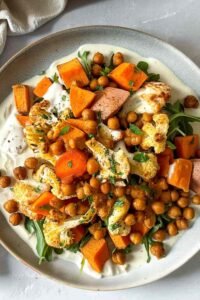 Colorful glow bowl recipe with roasted cauliflower, carrots, sweet potato, and crispy chickpeas topped with creamy tahini yogurt sauce