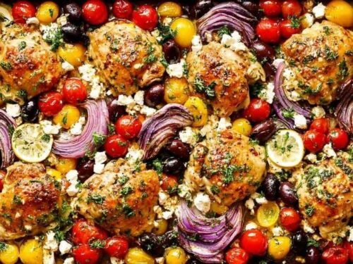Greek sheet pan chicken with roasted vegetables, kalamata olives, and crumbled feta on a rimmed baking sheet