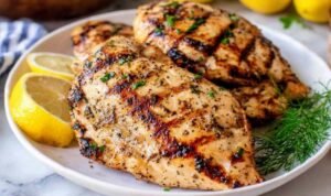 Grilled Chicken Breast Juicy sliced grilled chicken breast on a white plate with visible grill marks and fresh lemon wedges