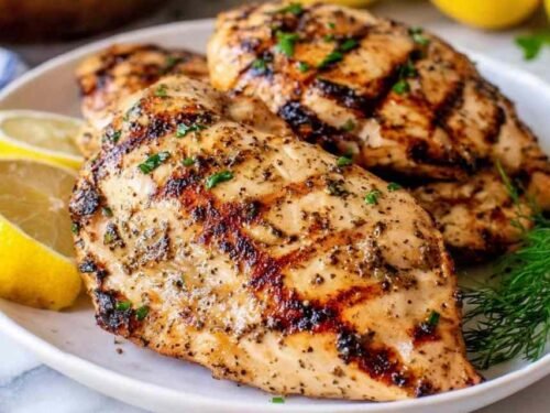 Juicy sliced grilled chicken breast on a white plate with visible grill marks and fresh lemon wedges