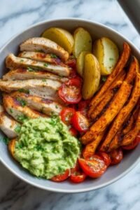 Grilled herb chicken bowl with sweet potato fries, avocado salsa, and quinoa served in a white bowl