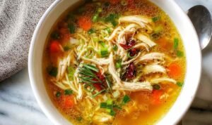 A bowl of Healing Ginger Garlic Chicken Noodle Soup with tender chicken, egg noodles, sliced carrots, and fresh parsley garnish