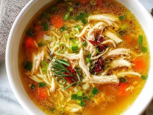 A bowl of Healing Ginger Garlic Chicken Noodle Soup with tender chicken, egg noodles, sliced carrots, and fresh parsley garnish