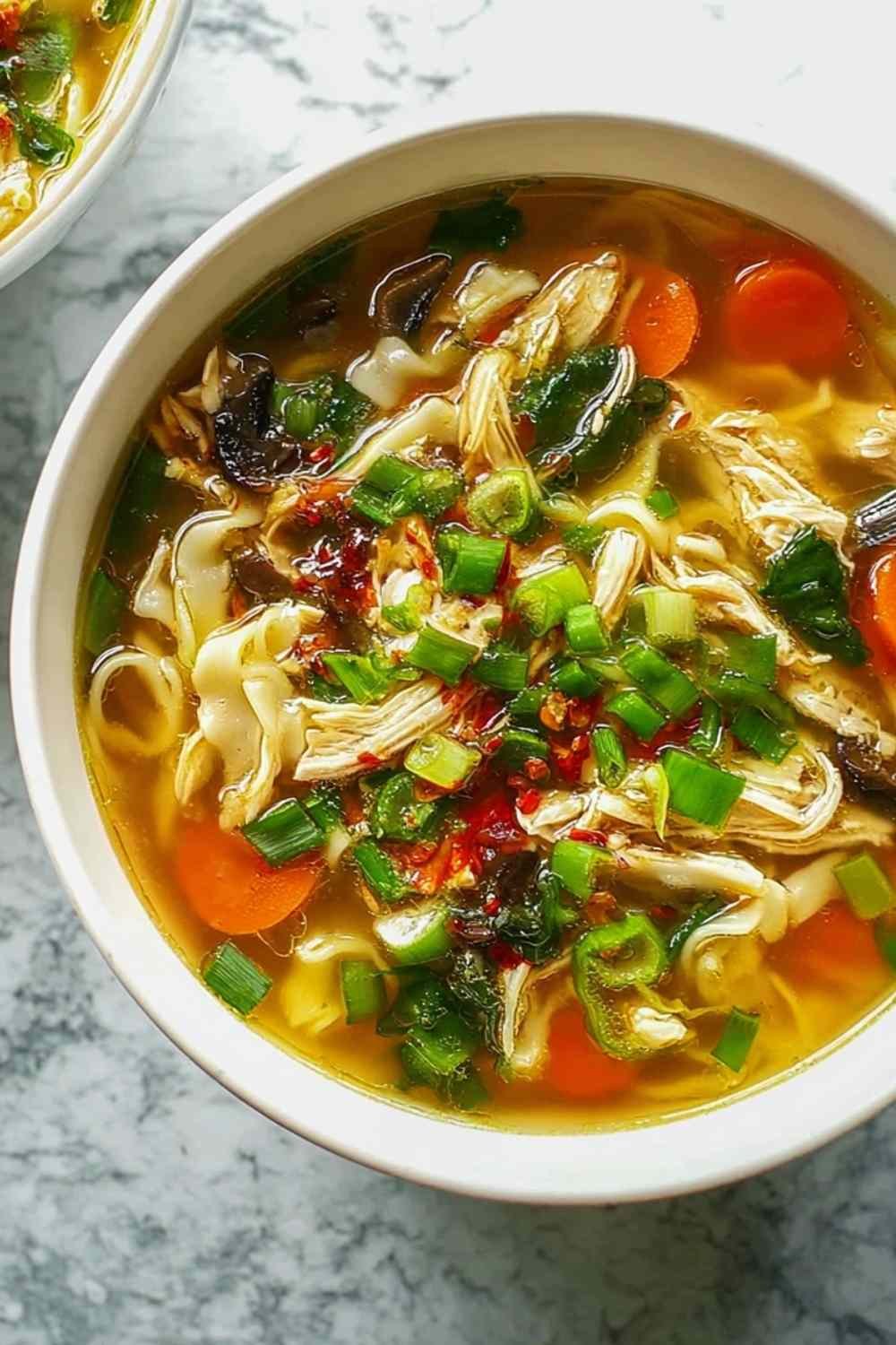 A bowl of Healing Ginger Garlic Chicken Noodle Soup with tender chicken, egg noodles, sliced carrots, and fresh parsley garnish