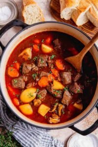 Easy beef stew recipe simmering in a Dutch oven with tender beef, carrots, and potatoes in a rich red wine broth