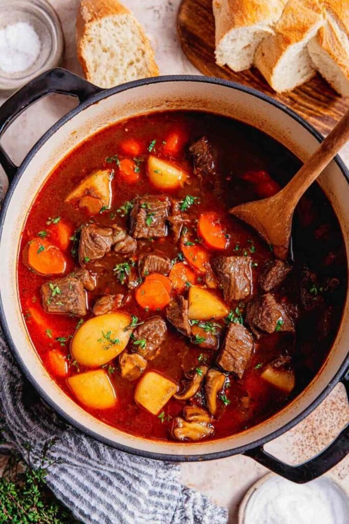 Easy beef stew recipe simmering in a Dutch oven with tender beef, carrots, and potatoes in a rich red wine broth