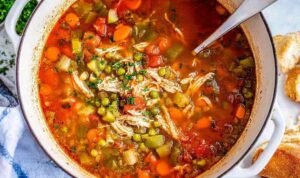 Chicken Vegetable Soup A bowl of homemade chicken vegetable soup with shredded chicken, carrots, green beans, peas, and potatoes in a golden herb broth, topped with fresh parsley