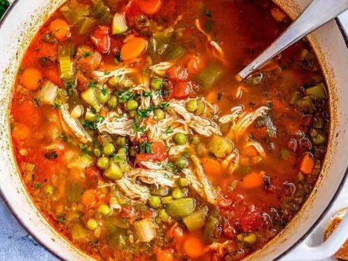 A bowl of homemade chicken vegetable soup with shredded chicken, carrots, green beans, peas, and potatoes in a golden herb broth, topped with fresh parsley