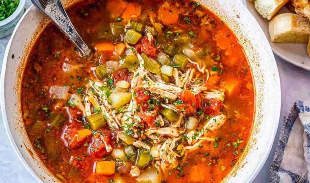 A bowl of homemade chicken vegetable soup with shredded chicken, carrots, green beans, peas, and potatoes in a golden herb broth, topped with fresh parsley