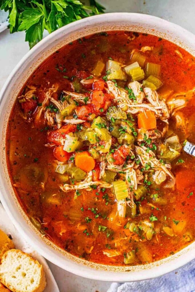 A bowl of homemade chicken vegetable soup with shredded chicken, carrots, green beans, peas, and potatoes in a golden herb broth, topped with fresh parsley