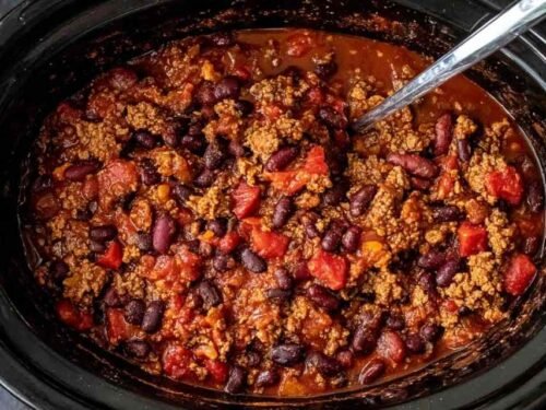 A hearty bowl of slow cooker chili topped with shredded cheddar cheese, sour cream, and sliced avocado