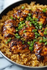 Honey BBQ chicken rice in a large skillet with golden chicken thighs, fluffy rice, and mixed vegetables garnished with chopped green onions