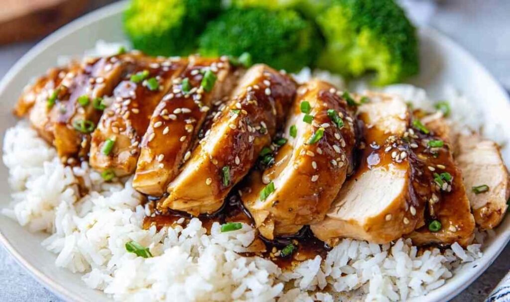 Sliced honey garlic Instant Pot chicken breast served over white rice with steamed broccoli and glossy sauce drizzled on top