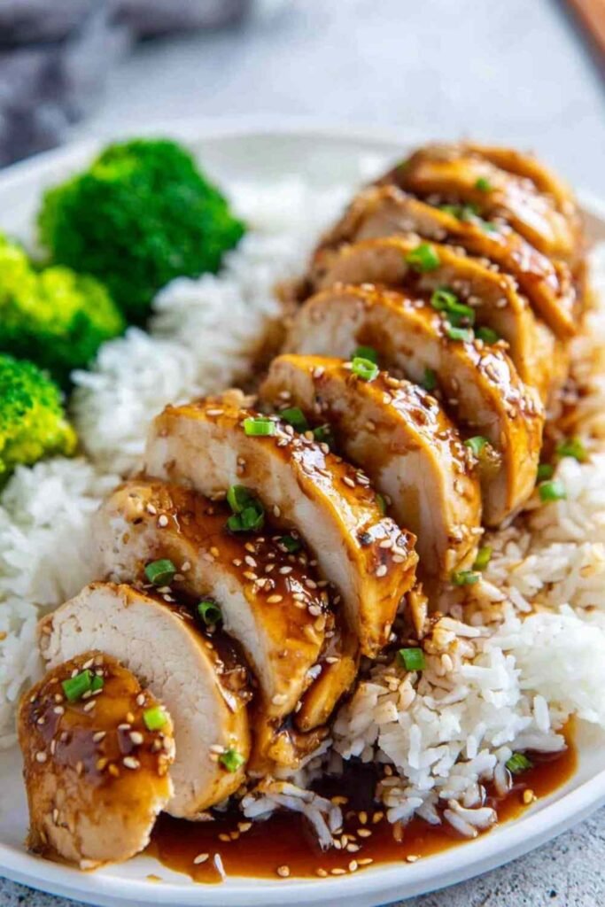 Sliced honey garlic Instant Pot chicken breast served over white rice with steamed broccoli and glossy sauce drizzled on top