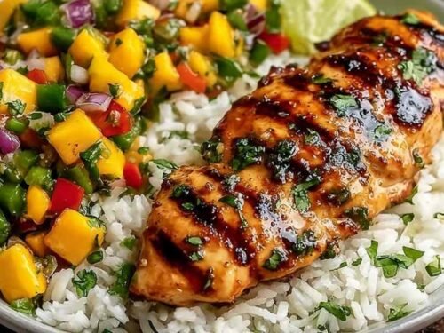 Sliced honey lime chicken topped with fresh mango salsa served over cilantro rice on a white plate