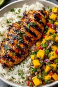 Sliced honey lime chicken topped with fresh mango salsa served over cilantro rice on a white plate