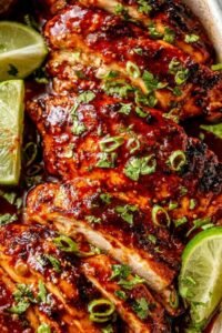 Honey sriracha chicken breasts in a baking dish coated in sticky sweet and spicy glaze garnished with sesame seeds and lime