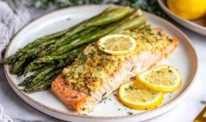 Four lemon garlic baked salmon fillets in a parchment-lined baking dish topped with fresh herbs
