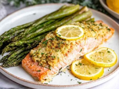 Four lemon garlic baked salmon fillets in a parchment-lined baking dish topped with fresh herbs