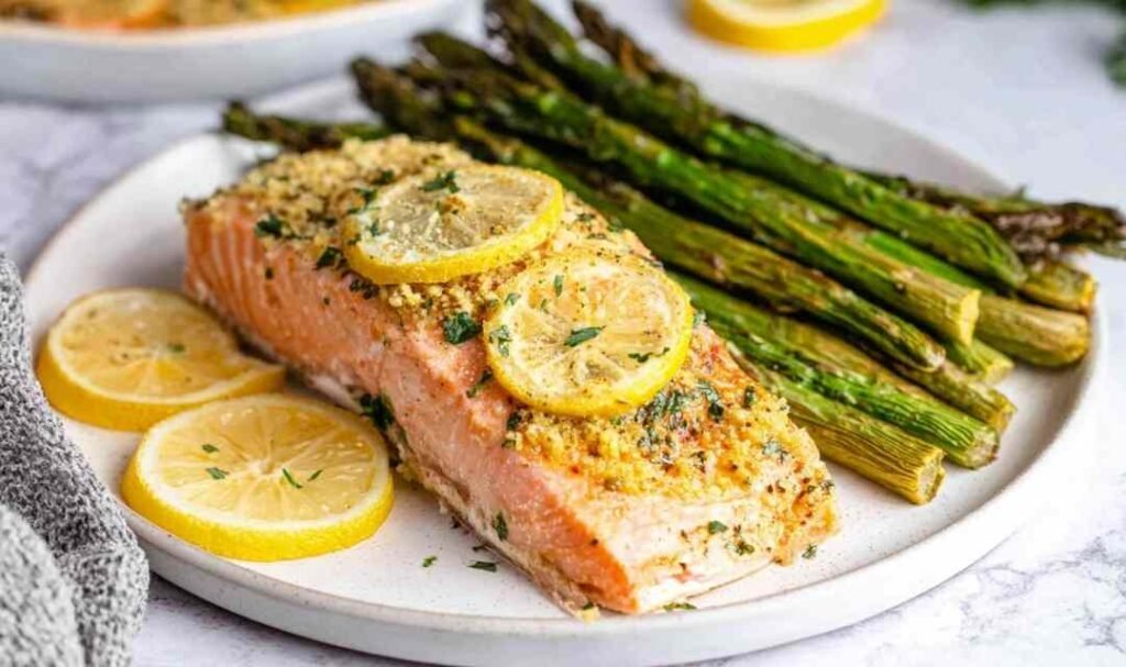 Four lemon garlic baked salmon fillets in a parchment-lined baking dish topped with fresh herbs