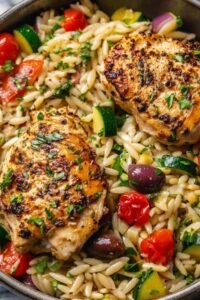 Mediterranean chicken orzo with sliced chicken, baby spinach, and sun-dried tomatoes in a large skillet