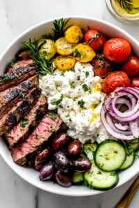 Mediterranean Steak Bowl with sliced grilled sirloin, cherry tomatoes, cucumber, kalamata olives, feta, and homemade tzatziki over brown rice