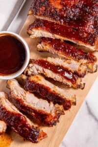 Rack of oven baked ribs sliced and coated in caramelized BBQ sauce on a cutting board