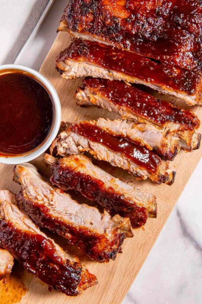 Rack of oven baked ribs sliced and coated in caramelized BBQ sauce on a cutting board