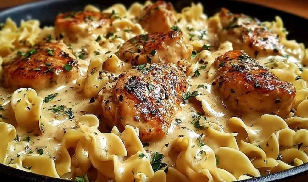 One pan creamy garlic butter chicken with egg noodles in a large skillet garnished with fresh parsley and Parmesan cheese