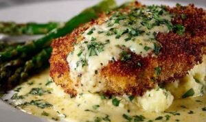 Parmesan crusted chicken cutlets on a plate covered in creamy garlic sauce with fresh parsley garnish