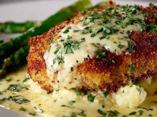 Parmesan crusted chicken cutlets on a plate covered in creamy garlic sauce with fresh parsley garnish