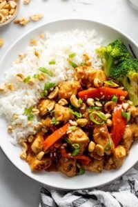 Crispy peanut butter chicken tossed in savory peanut sauce in a skillet with broccoli and carrots
