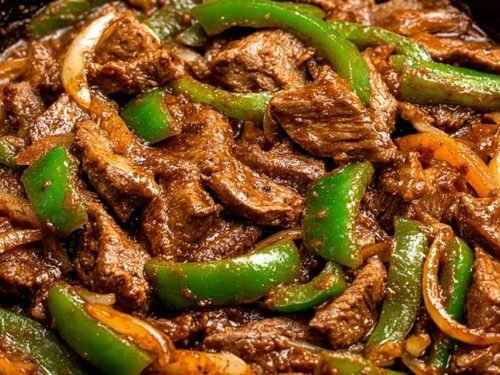 Pepper steak with tender ribeye strips, colorful bell peppers, and rich tomato beef sauce served over white rice with fresh green onion garnish