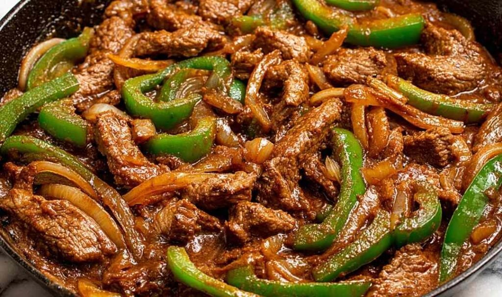 Pepper steak with tender ribeye strips, colorful bell peppers, and rich tomato beef sauce served over white rice with fresh green onion garnish