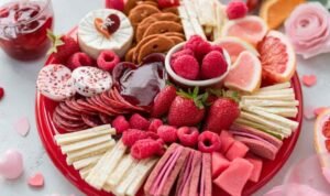 Pink and red themed board with strawberry cream cheese, raspberries, heart pepperoni, and red velvet cookies on a serving platter