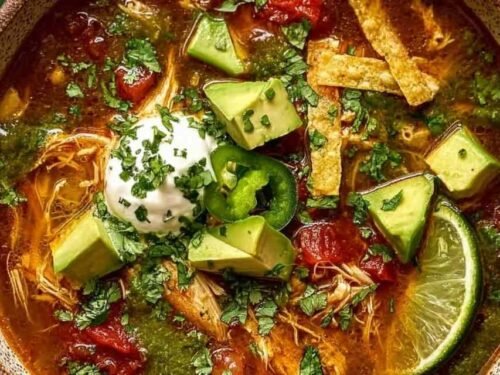 A bowl of poblano chicken tortilla soup topped with tortilla strips, diced avocado, shredded cheese, sour cream, and fresh cilantro