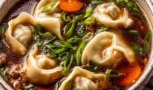 Potsticker soup in a bowl with beef dumplings, fresh greens, and chopped green onion garnish