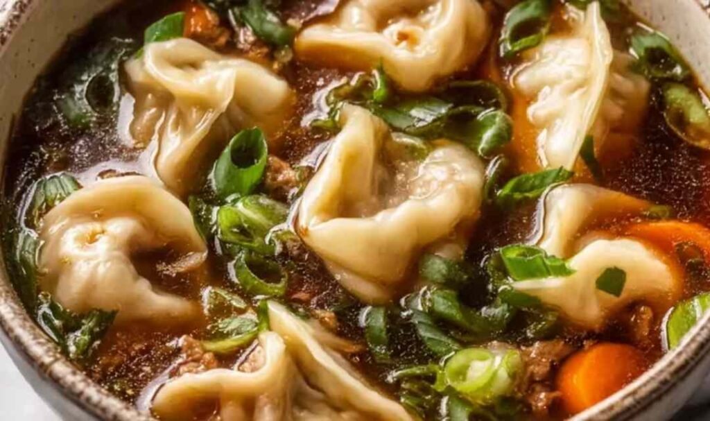 Potsticker soup in a bowl with beef dumplings, fresh greens, and chopped green onion garnish